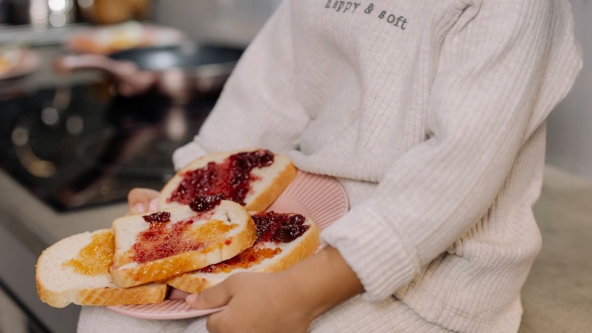A child in a cozy sweater holds a plate of jam sandwiches indoors.